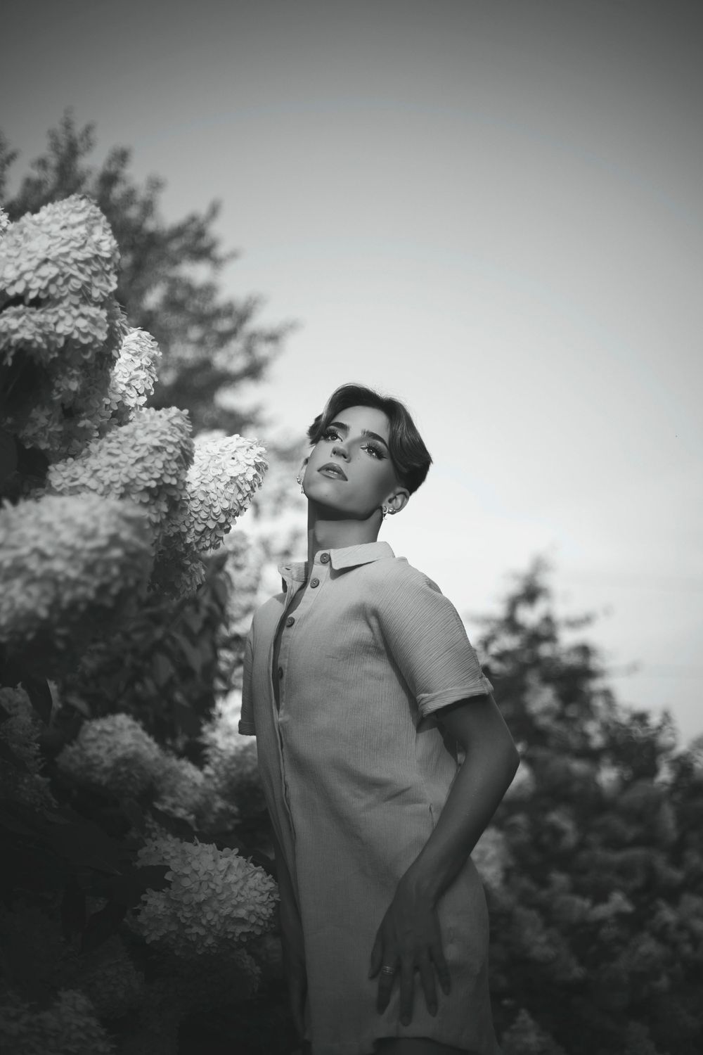 Artistic black and white portrait of someone posing against a blurred nature backdrop in a casual summer outfit.