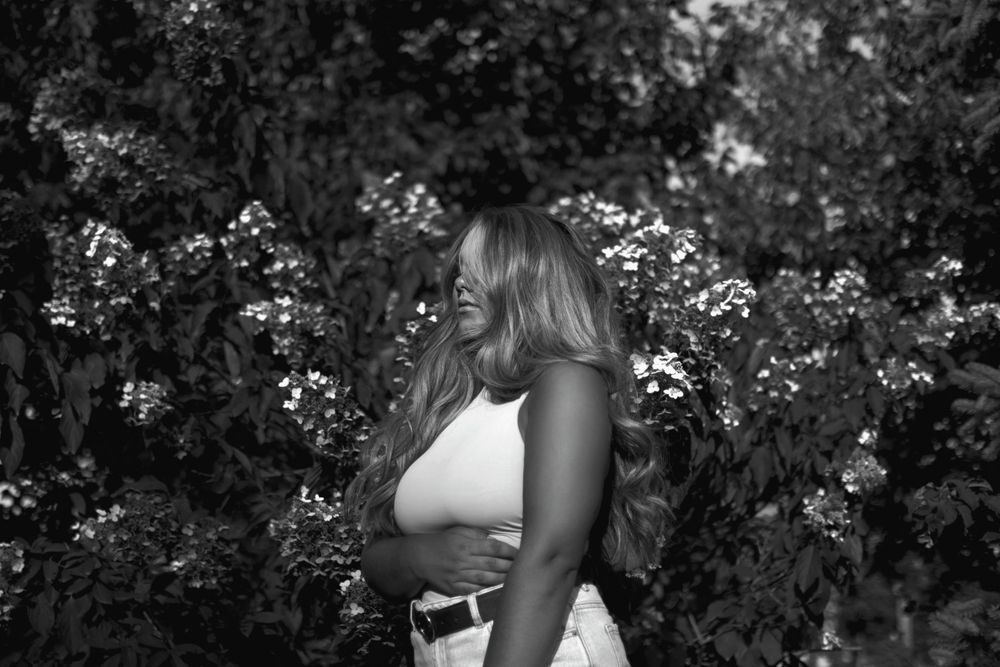 A side profile view of someone in a white top standing among flowering bushes in black and white photography.