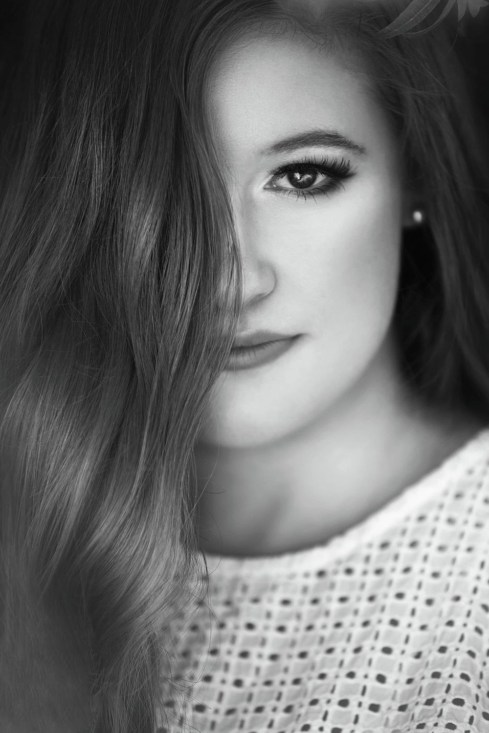 Black and white portrait photograph showing half a face with dramatic lighting wearing a white knit sweater.