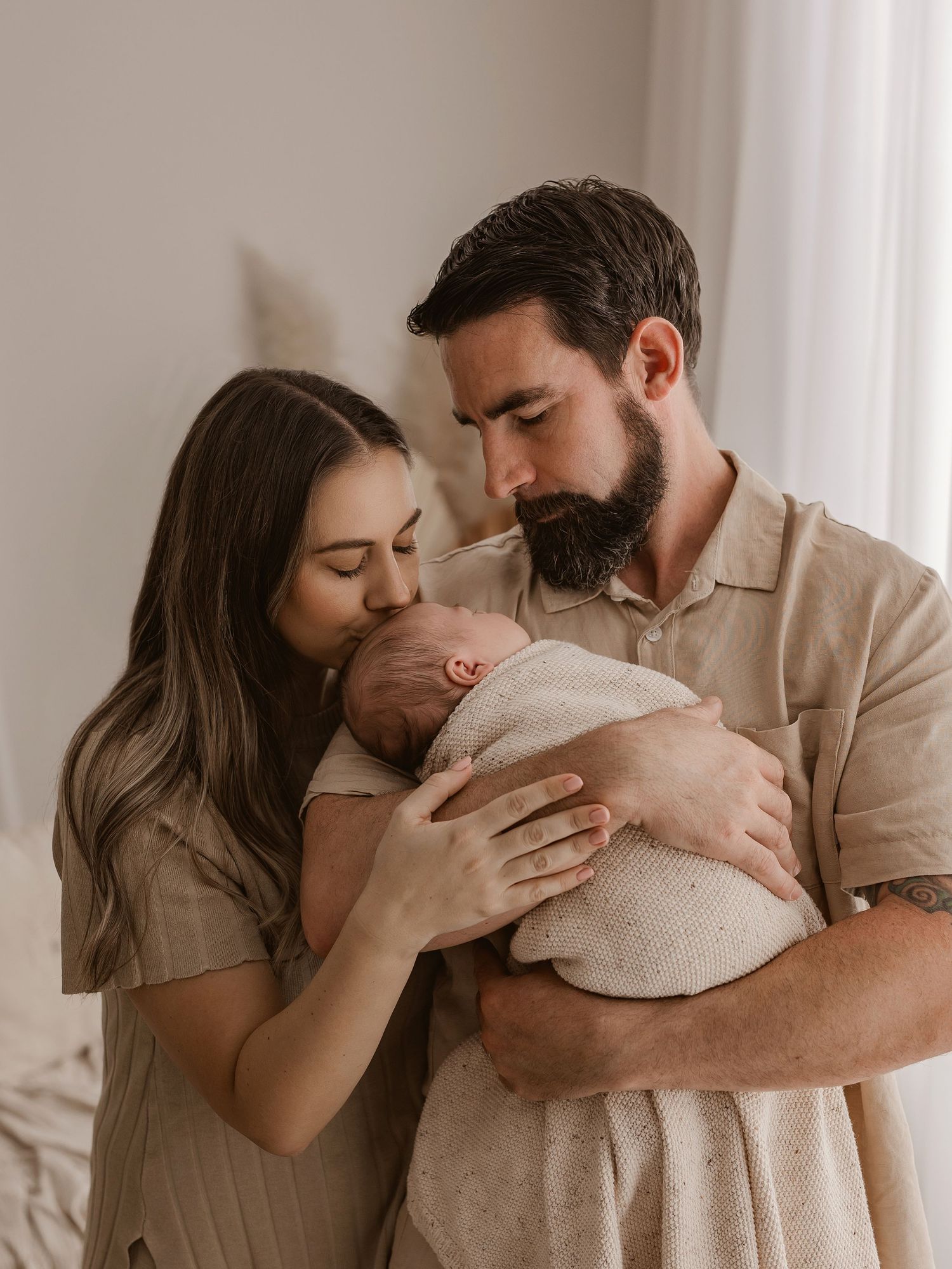 Parents sharing an intimate moment with their newborn in soft beige tones.