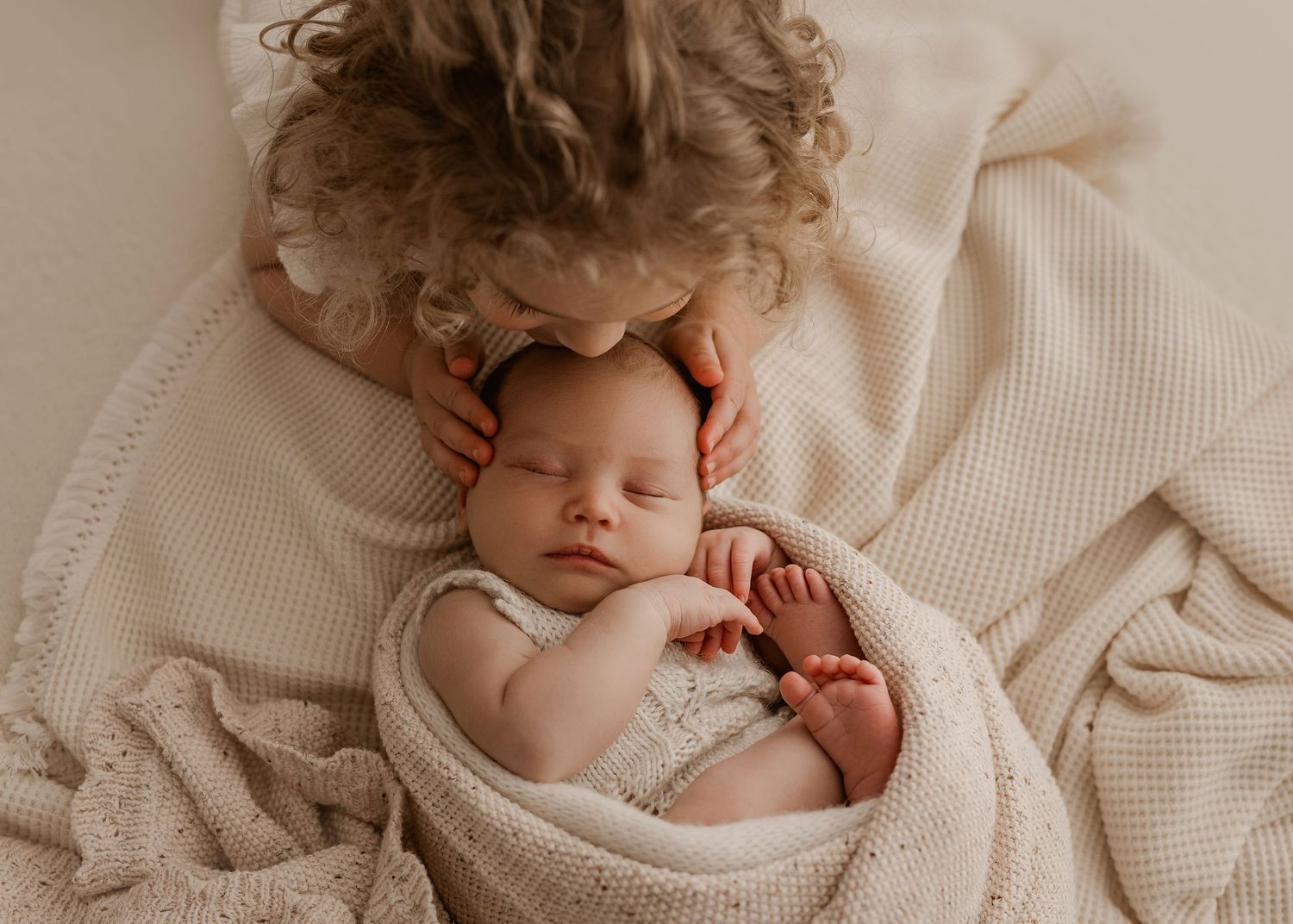 A sleeping newborn wrapped in cream-colored textiles with curly fabric details in soft natural light.