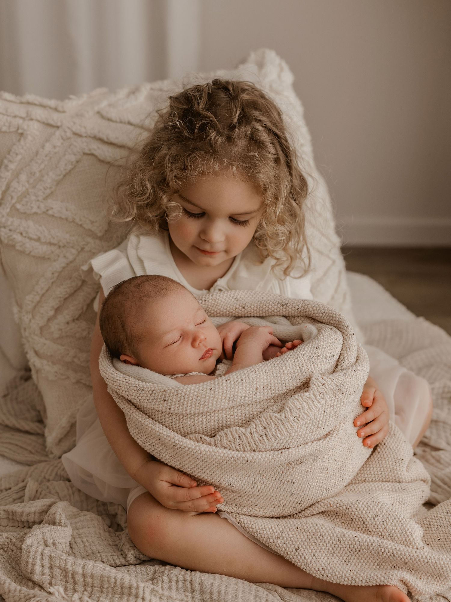 Tender moment with siblings cuddling on white textured bedding.