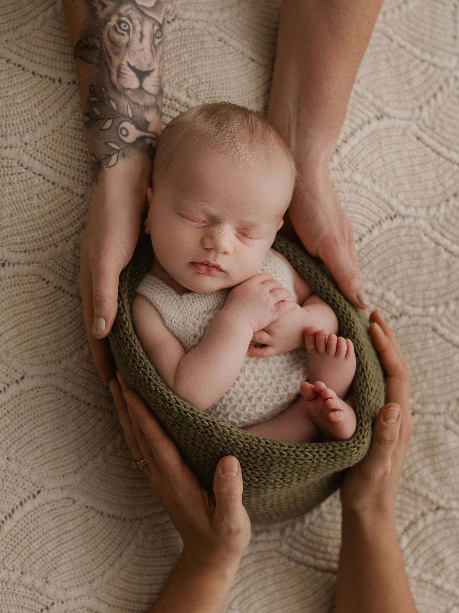 Gentle hands cradle a sleeping newborn in a knitted olive green nest.