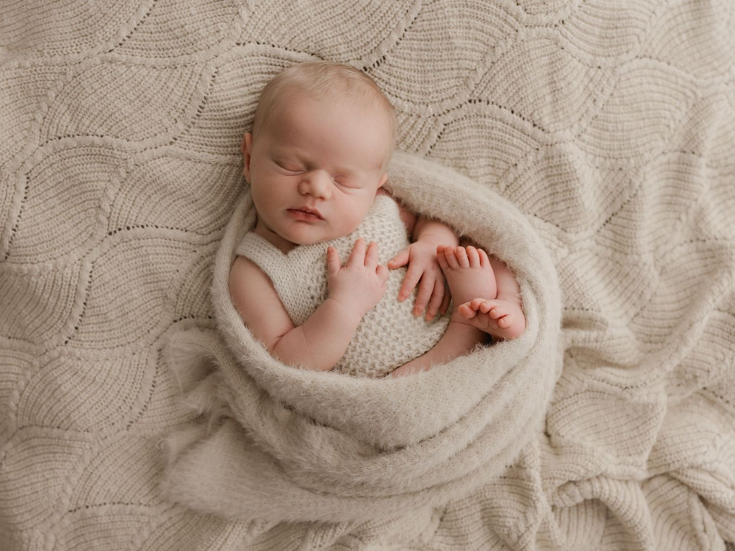 Peaceful newborn sleeping soundly in wrapped white textured blanket.