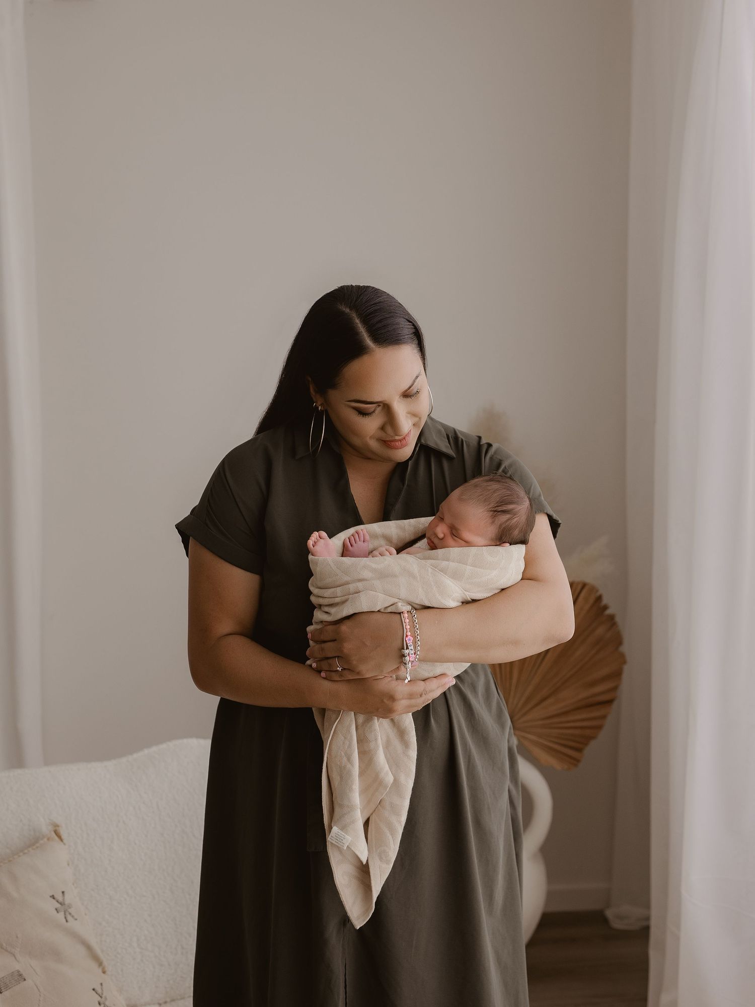 A tender moment captured in soft light as a parent in a dark dress cradles their sleeping newborn wrapped in light fabric.