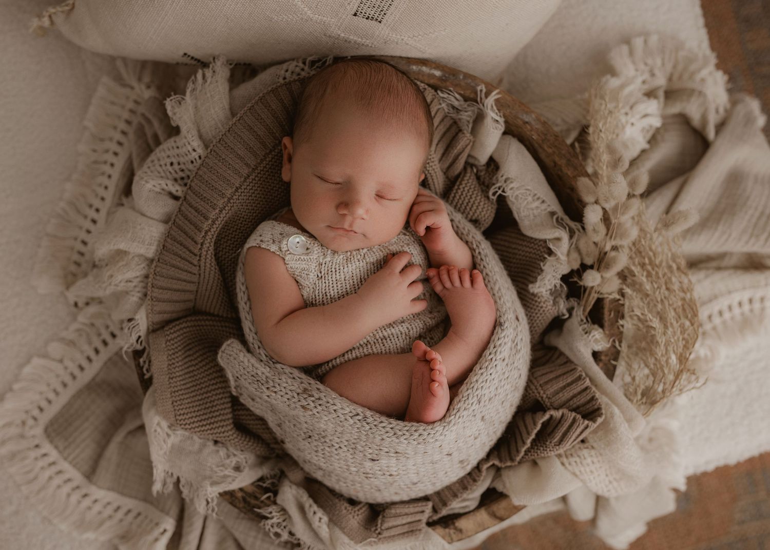 Newborn baby sleeping peacefully on textured cream blankets and lace.