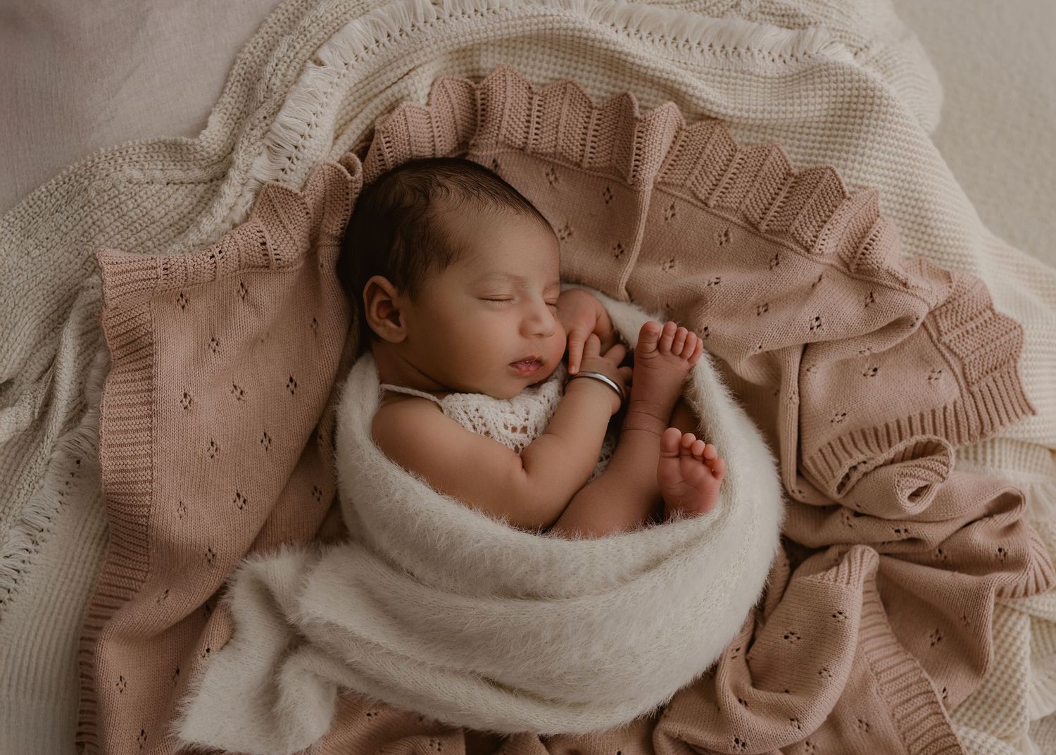 Newborn resting peacefully in a cozy cream-colored nest.