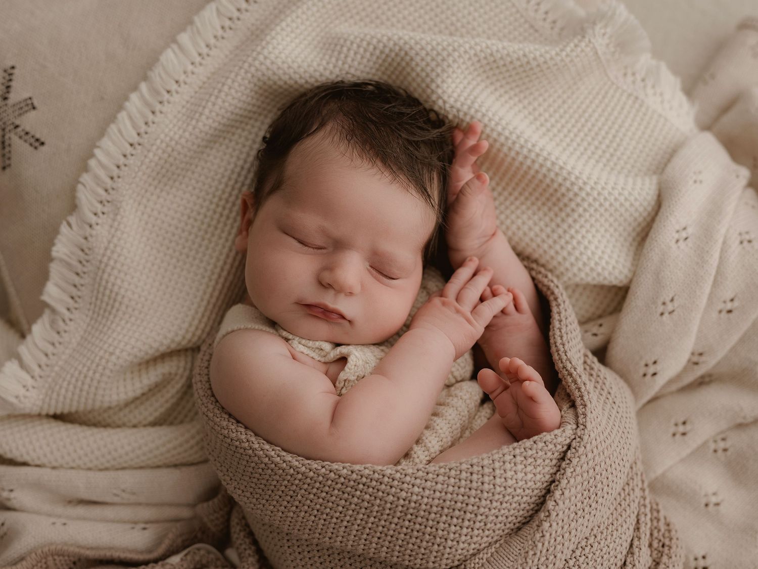 A sleeping newborn baby wrapped in a cozy knit blanket in muted neutral tones.