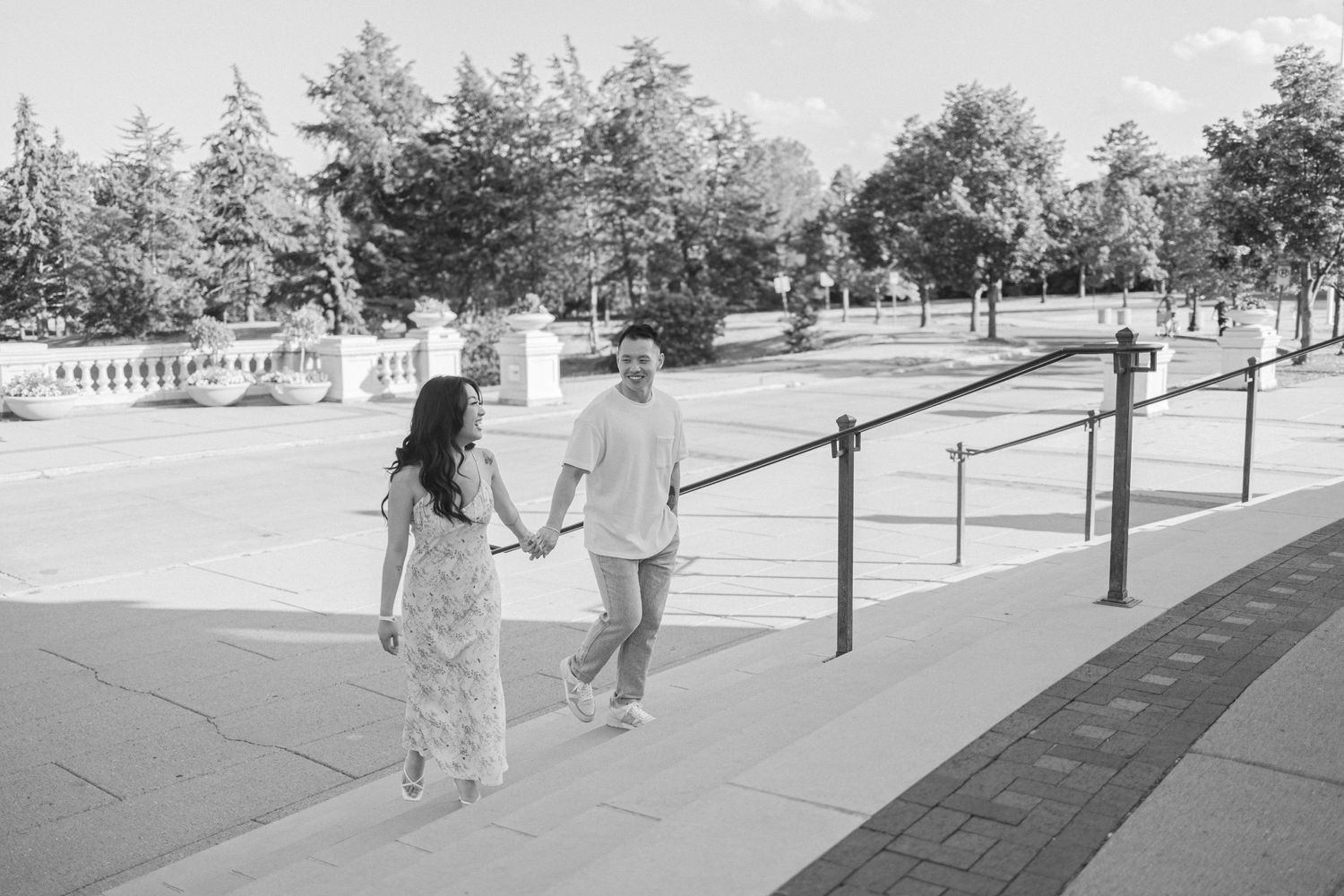 Black and white photo of couple ascending stairs while holding hands outdoors.