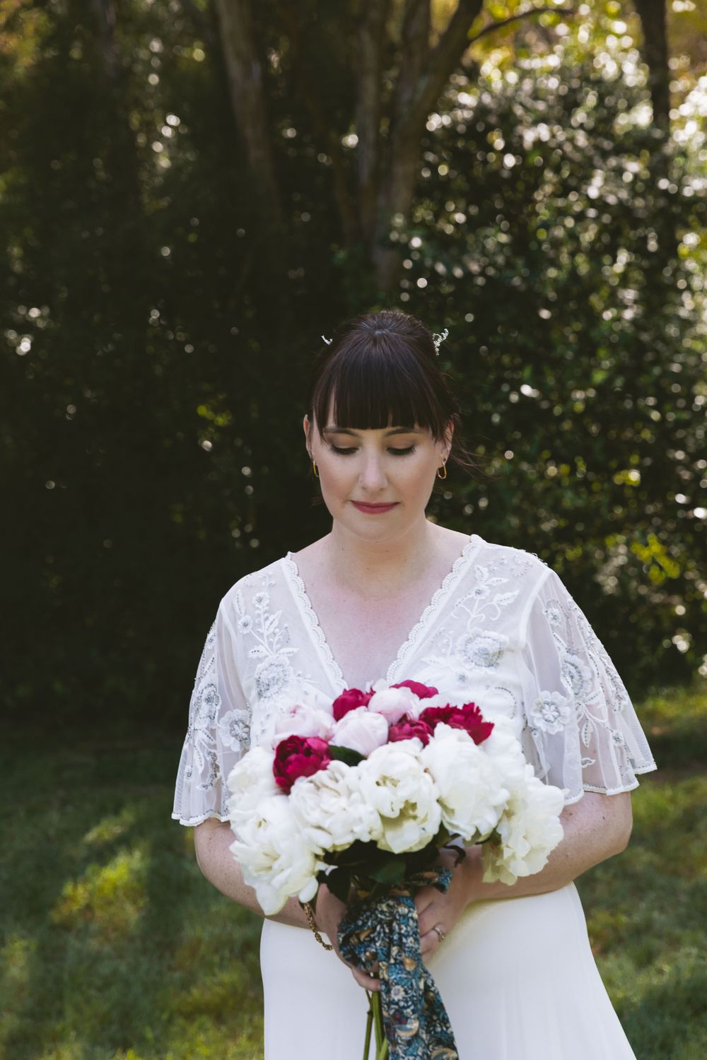 A lush garden wedding scene with a white dress and vibrant bouquet of red and white flowers.
