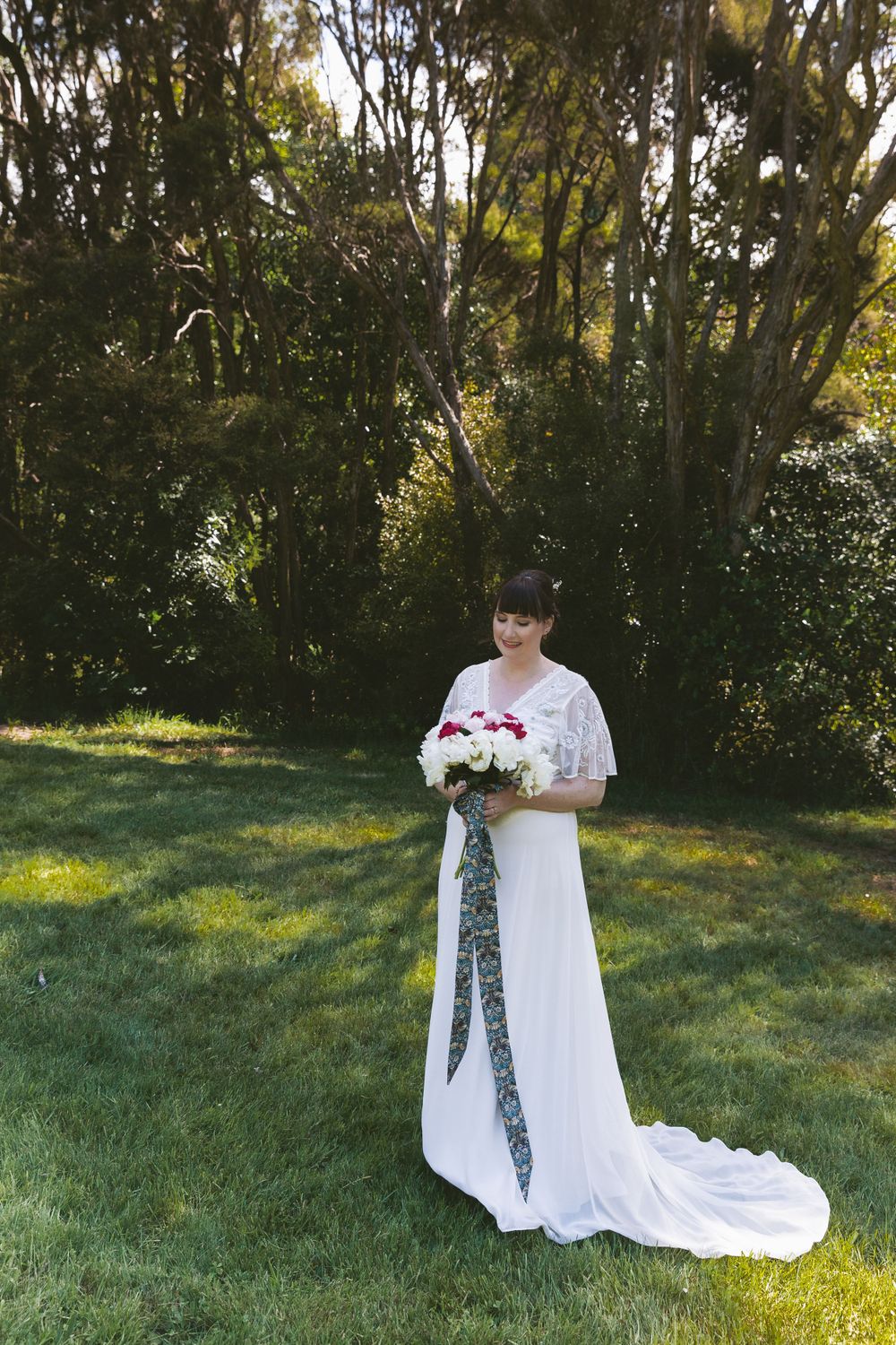An elegant wedding dress with flutter sleeves photographed in a sunlit garden setting.