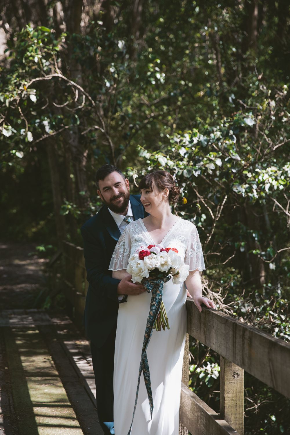 A romantic moment captured on a wooden bridge surrounded by lush greenery.