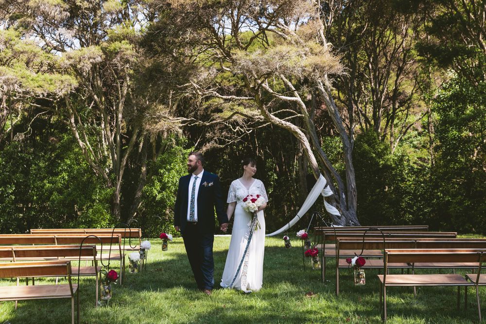 A woodland wedding ceremony setup with wooden benches and natural tree arch.