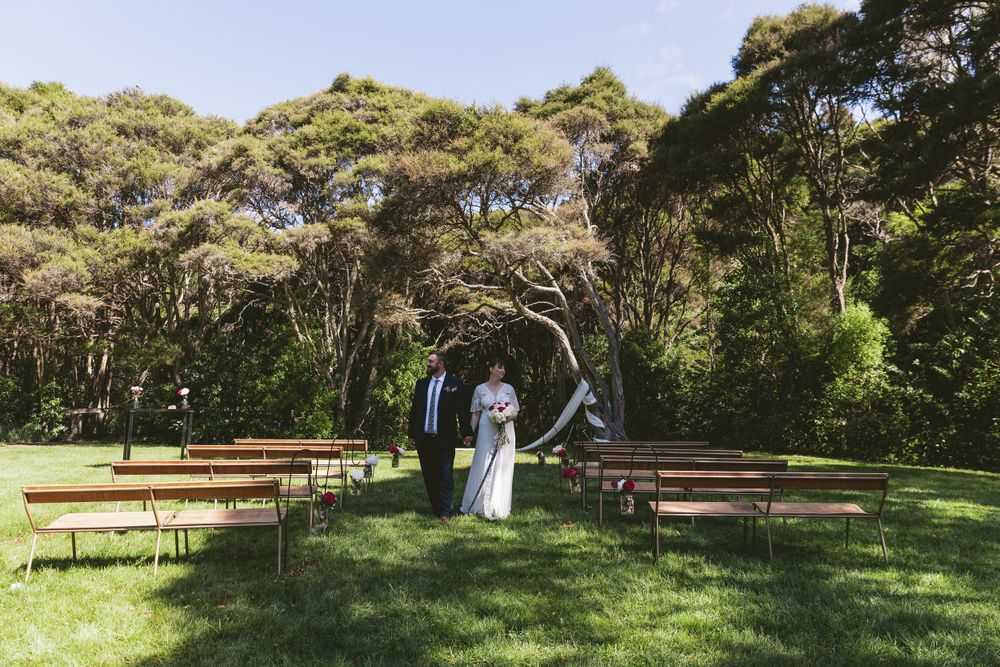 An outdoor wedding venue with rows of wooden benches leading to a natural tree arch.