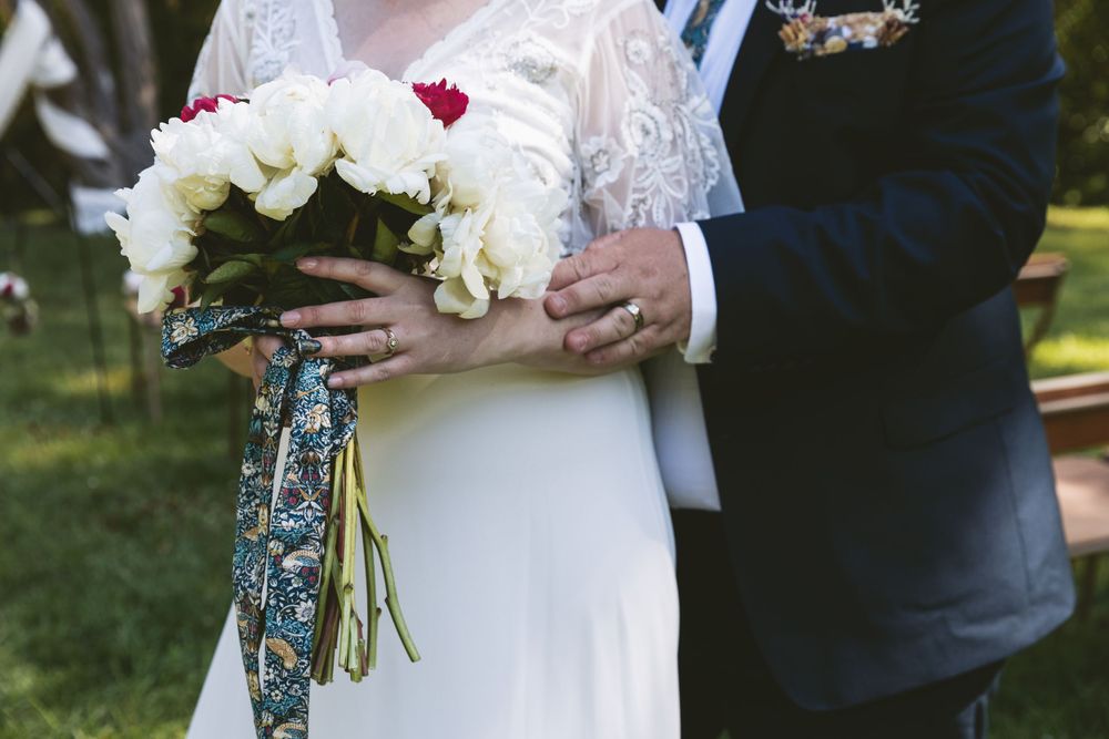 Close up of hands holding a white and red bouquet with decorative blue floral ribbon.