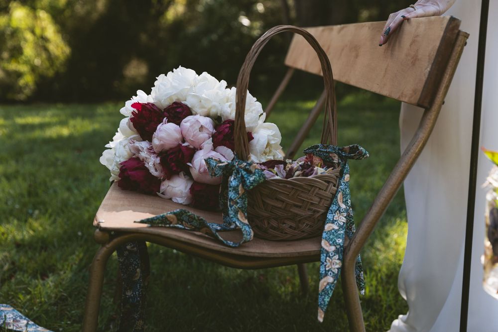 Wedding bouquet with white and burgundy flowers rests on vintage wooden chair.
