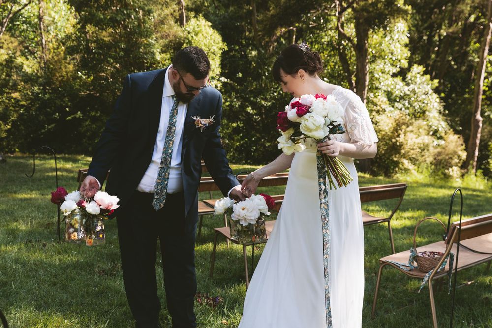 Newlyweds in wedding attire stand together outdoors holding matching bouquets.