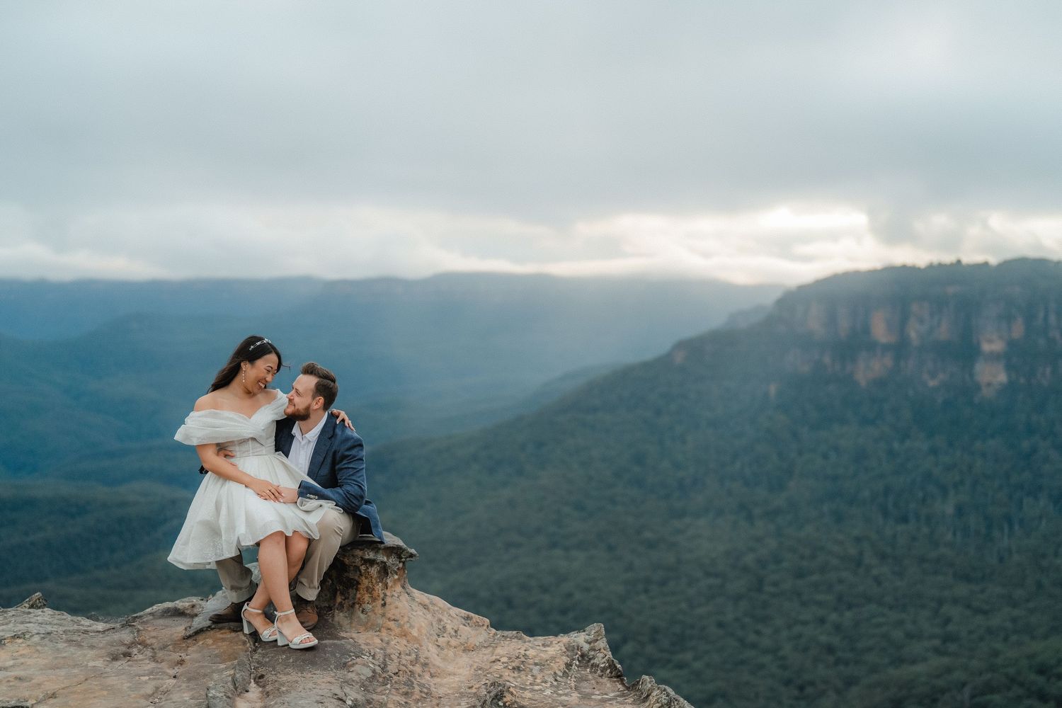 A romantic moment between newlyweds on a stone pier with a misty lake backdrop.