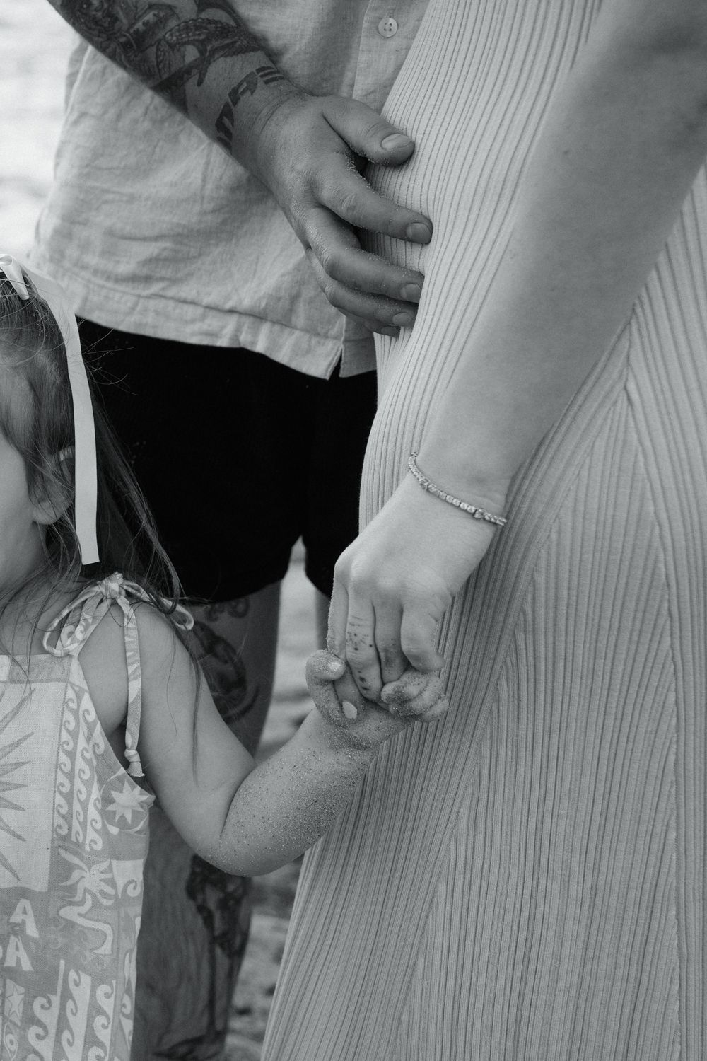 A black and white close-up photograph of hands tenderly holding onto each other against light colored clothing.