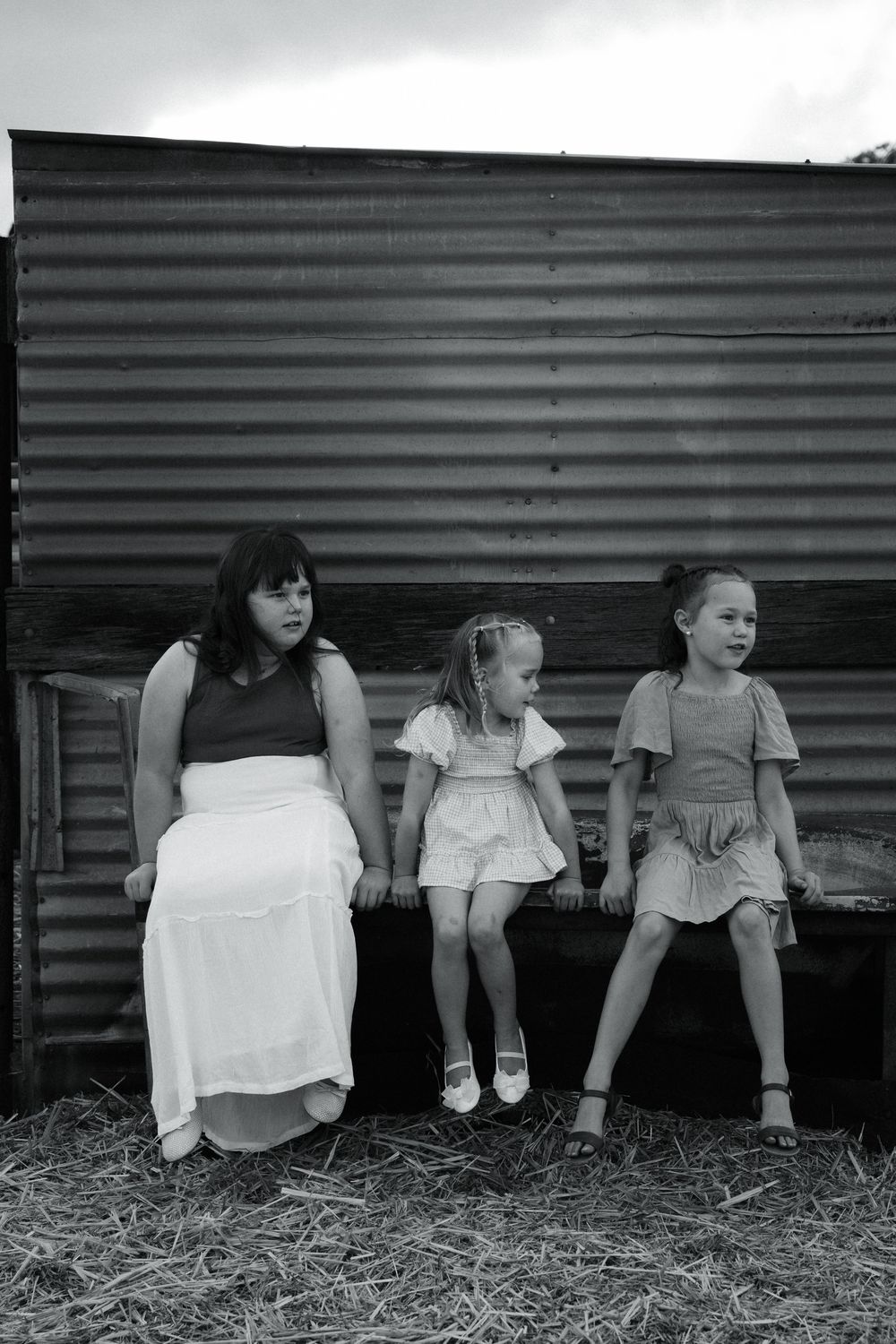Several people's legs and feet are shown dangling from a rustic barn or wooden structure, sitting in a line against a dark wall.