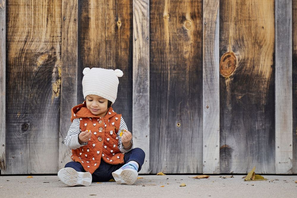 A baby in winter clothing sits adorably against weathered wooden panels.