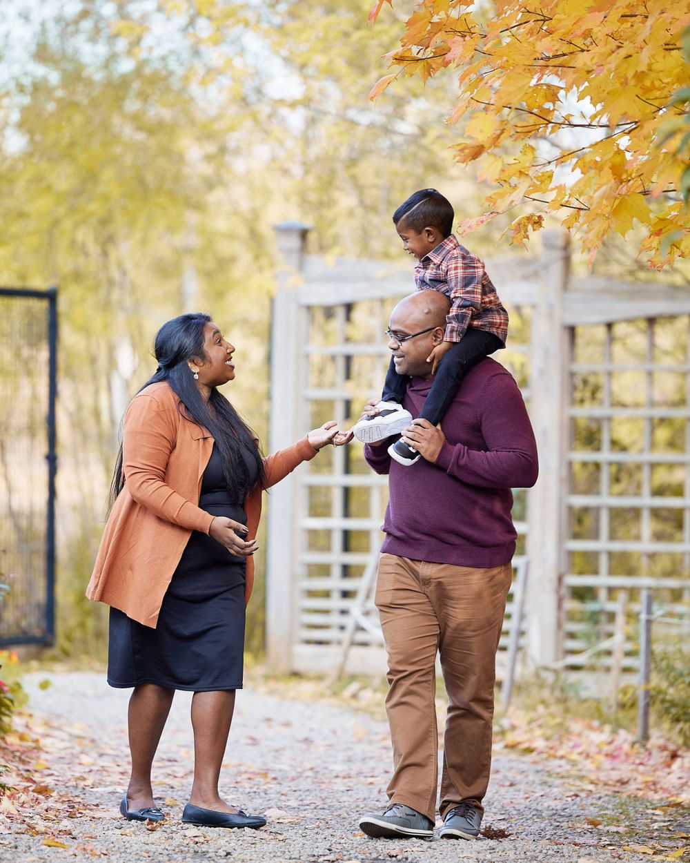 A family shares a lighthearted moment on an autumn path with golden foliage.