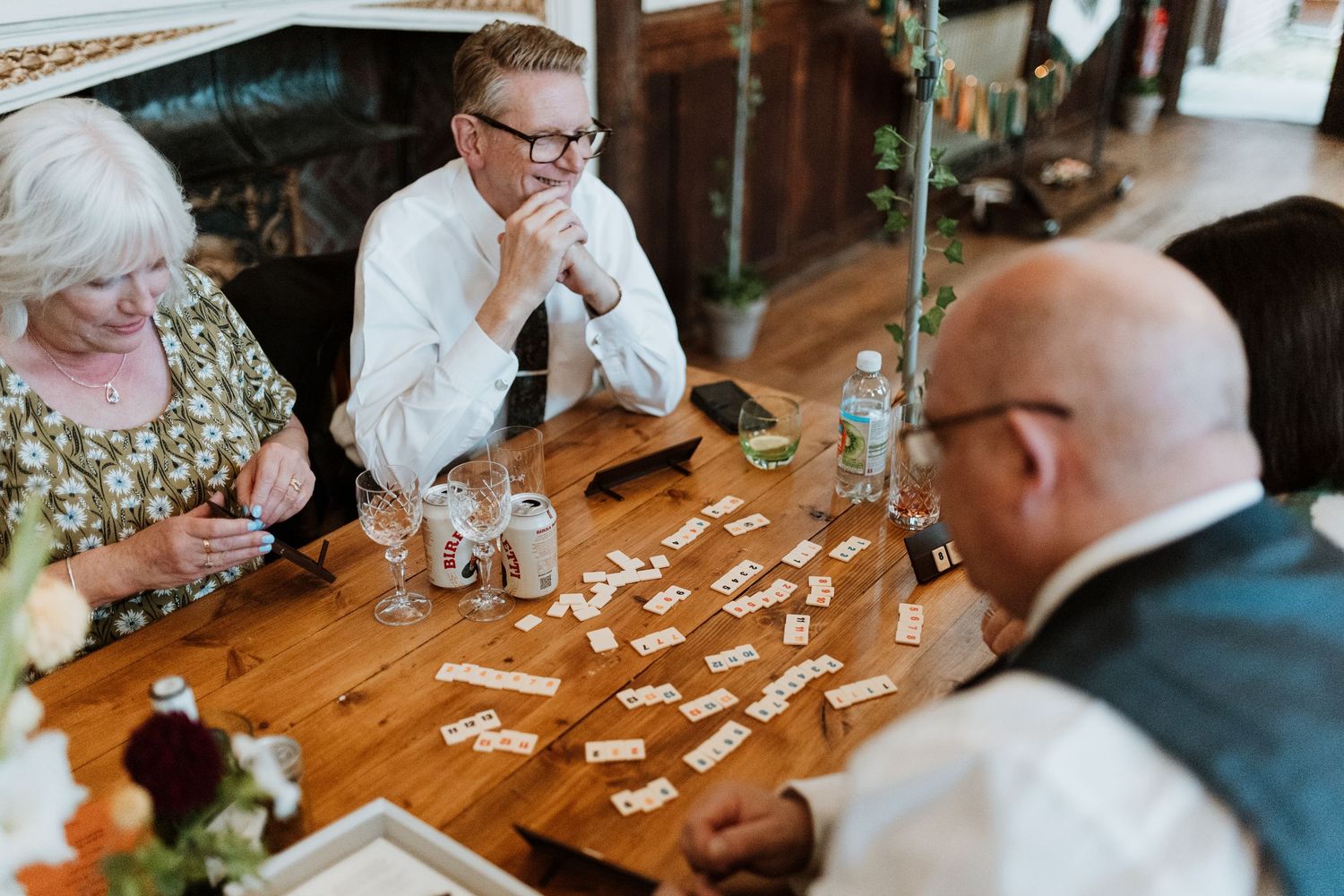 Group of people playing dominos together at a wooden table during a wedding reception.