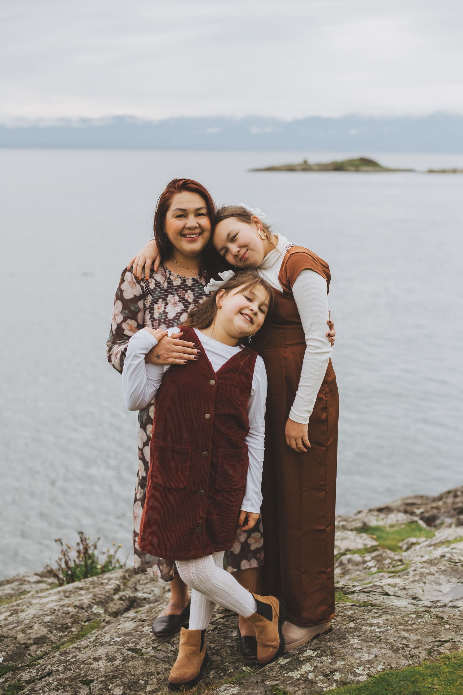Mother embracing her daughters on a cliffside overlooking the ocean.