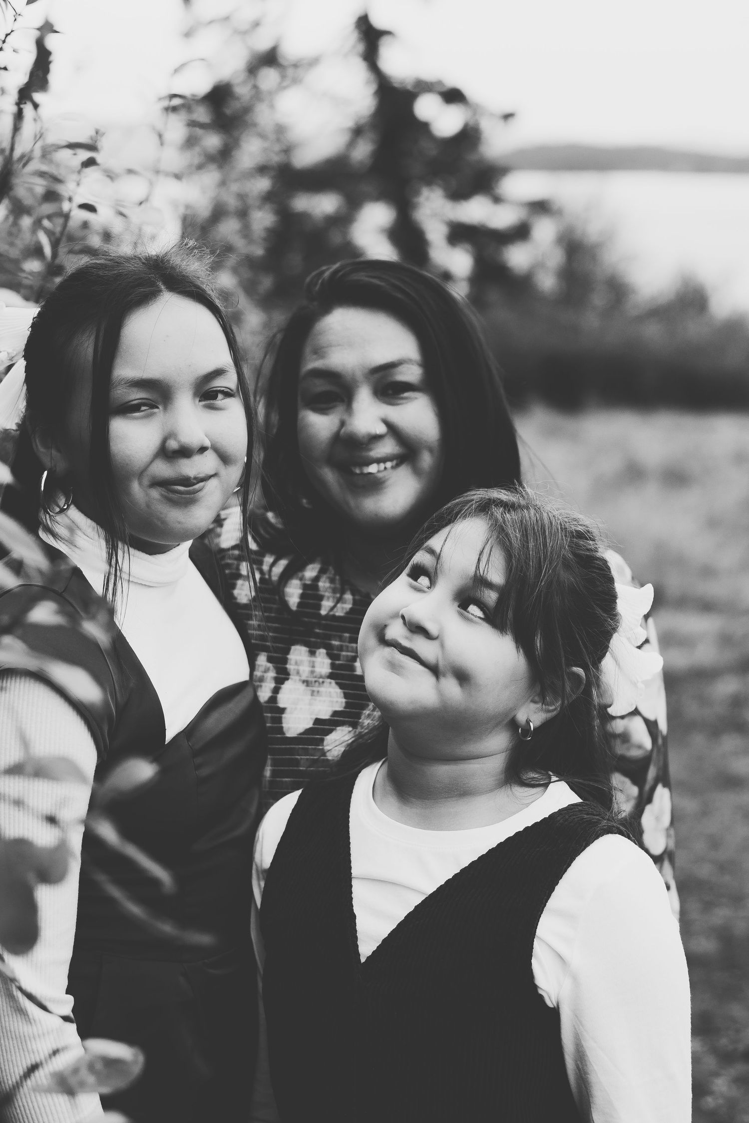 Mother and daughters share a loving moment outdoors in black and white.