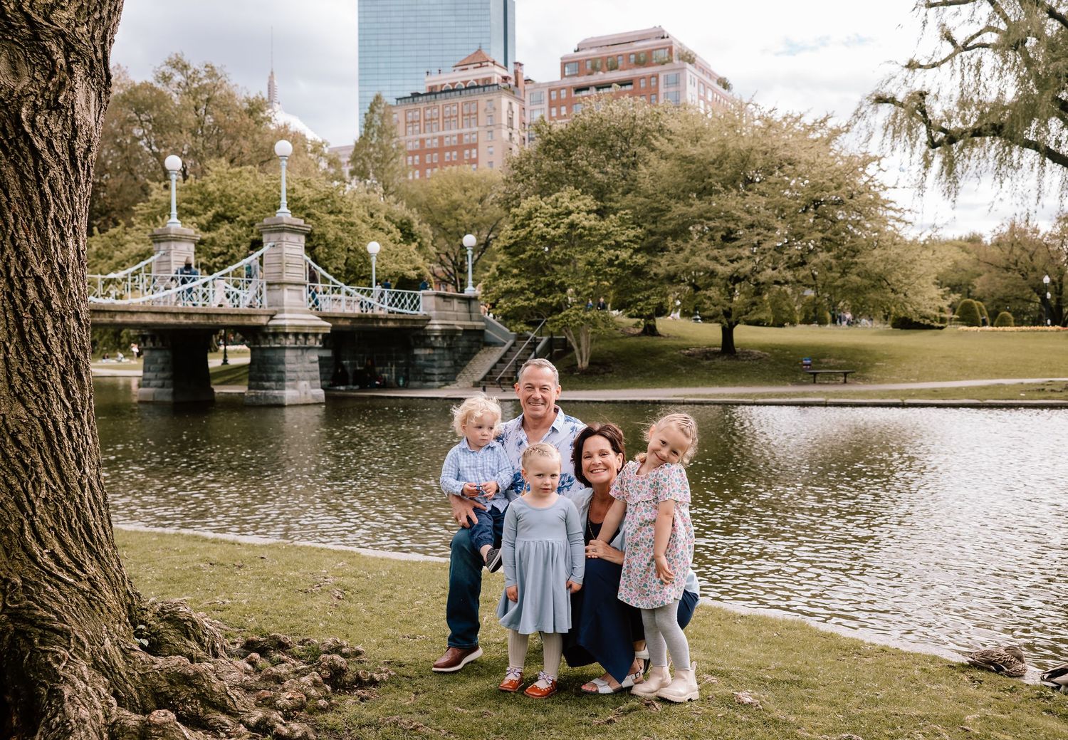 A scenic family photo session takes place in Boston Public Garden near a peaceful pond on a sunny autumn day.