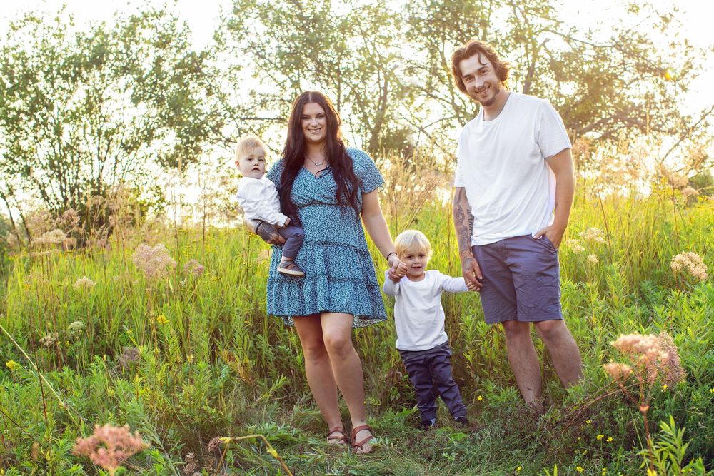 A small group stands together in a sunlit meadow with tall grass and wildflowers on a summer evening.