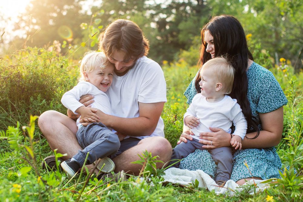 Family sitting together on a grassy meadow with wildflowers during golden sunset light.