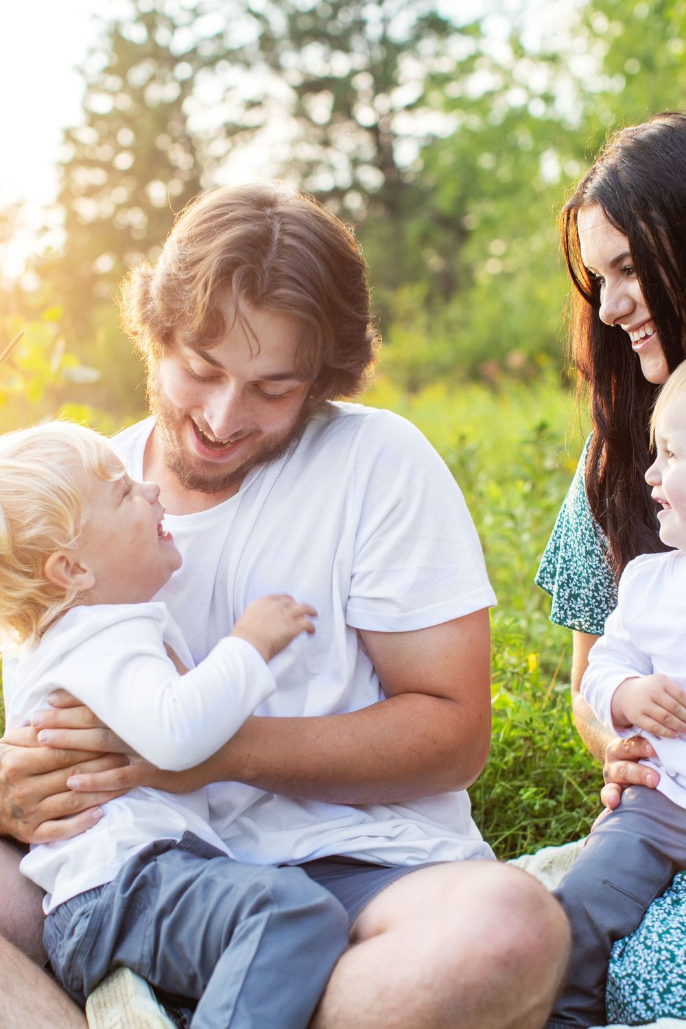 Family spending tender moments together outdoors on a sunny day in casual white attire.