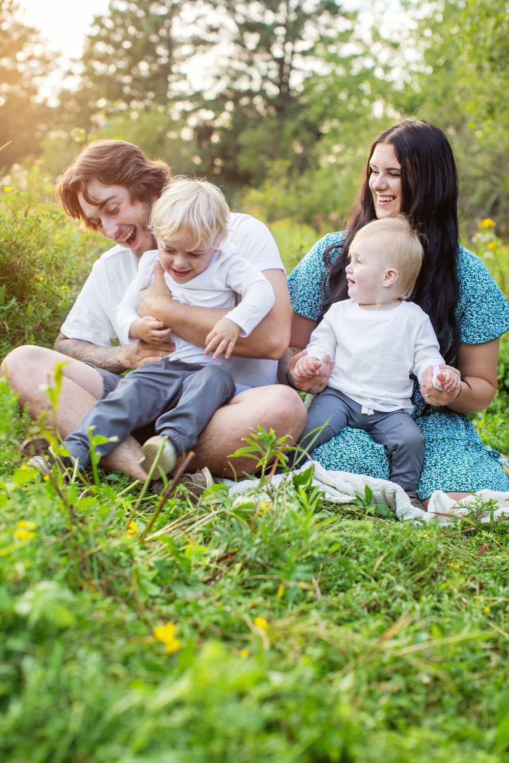 Family enjoying a sunny afternoon together while sitting on grass with yellow wildflowers in a serene outdoor setting.