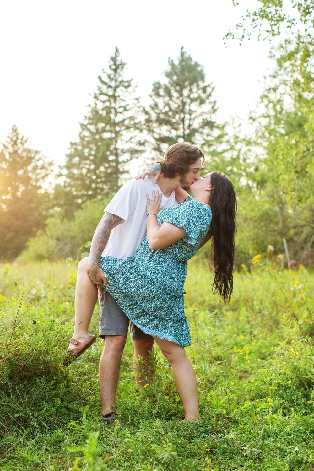 Romantic couple playfully posing in a sun-drenched meadow with green foliage and golden light.