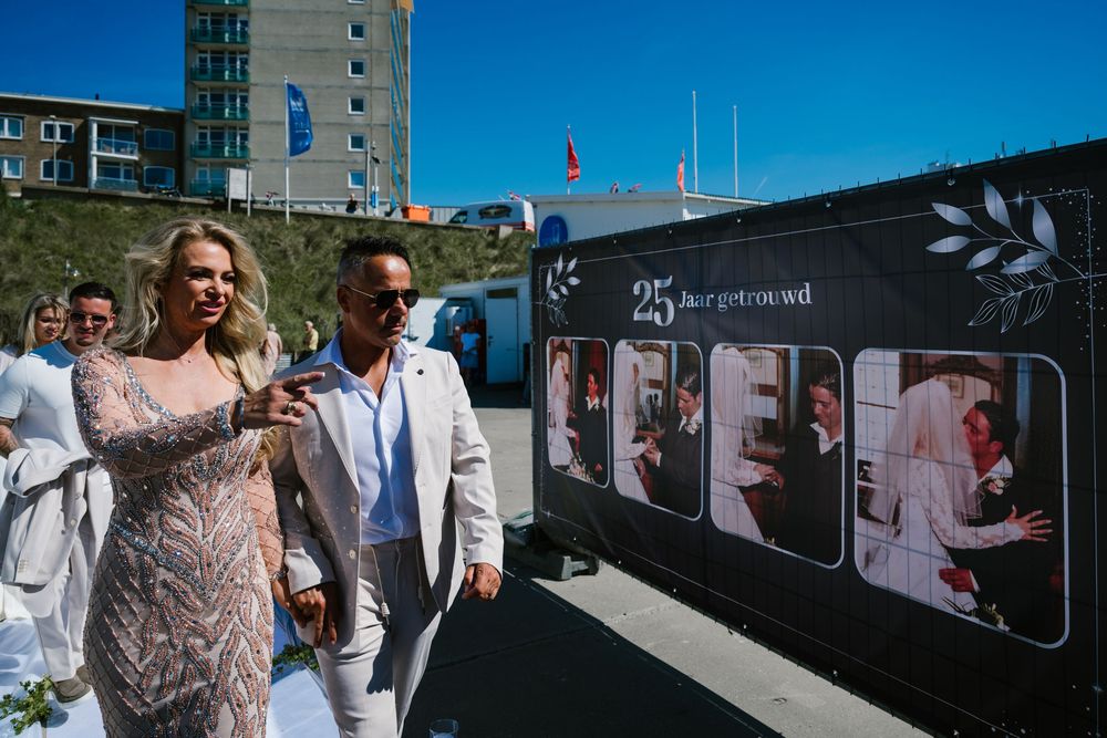 Wedding party walking past outdoor photo display wall under bright blue sky.
