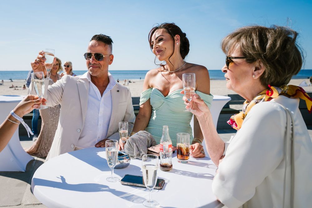 Group of people enjoying drinks and conversation at an outdoor beachside table.