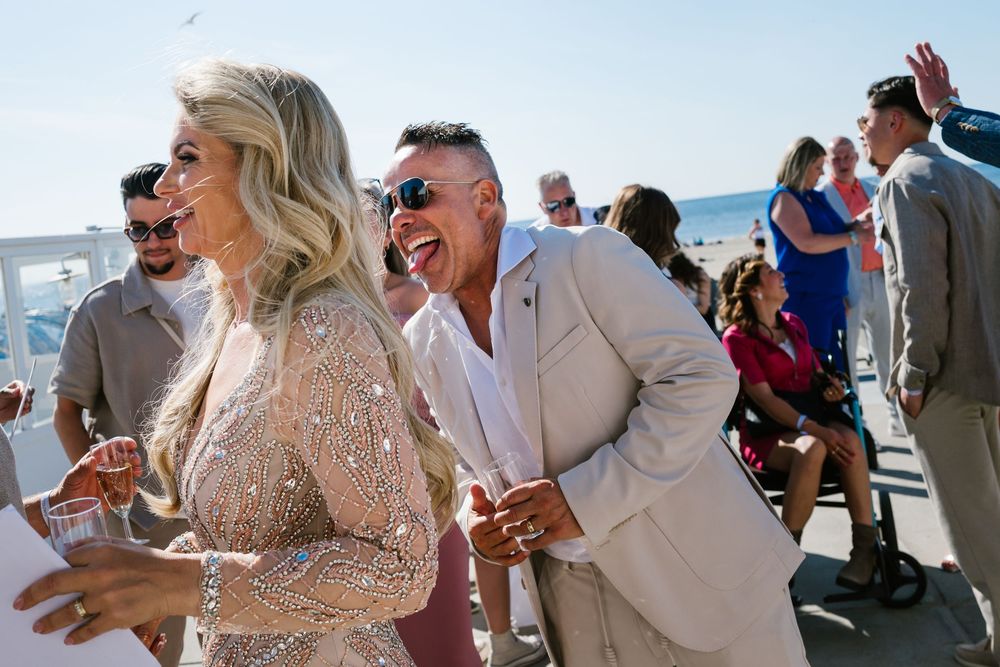 Wedding party dances and celebrates at a beach reception while dressed in beige and cream colored attire.