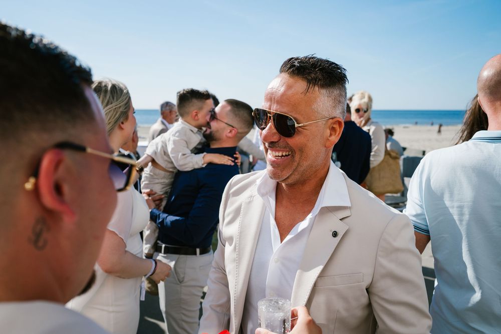 Wedding guests celebrate and embrace on a sunny beach with blue sky and ocean in the background.