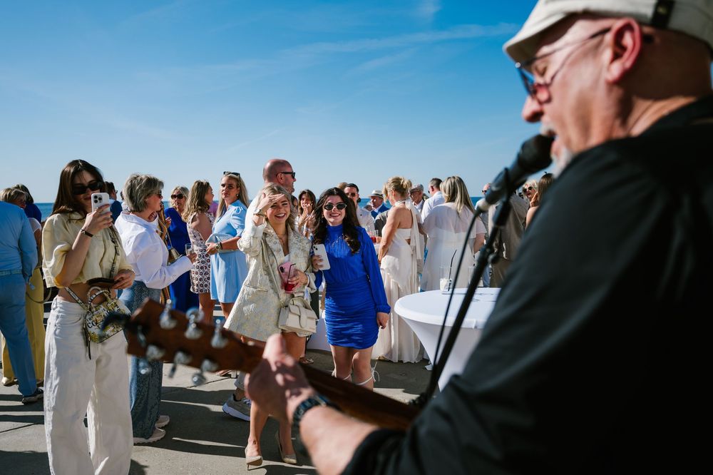 Live musician performs at a beachside outdoor event as guests gather to listen on a sunny day.