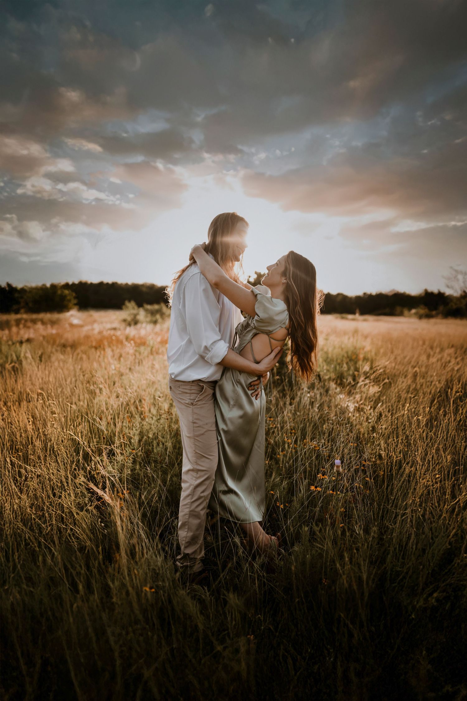 Engaged couple walking hand-in-hand through a golden grass field at sunset