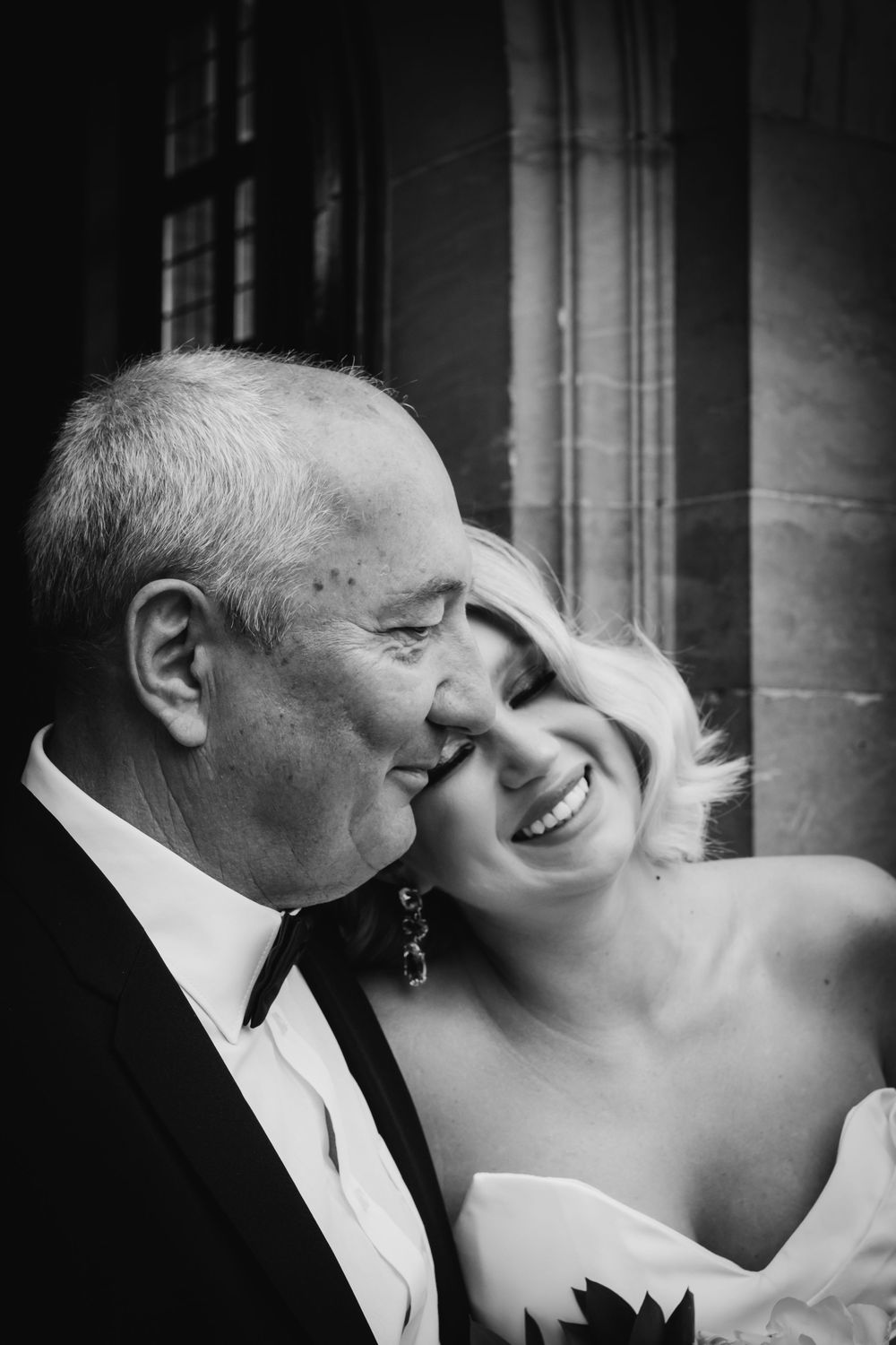 A heartwarming black and white wedding portrait showing a joyful couple sharing an intimate moment against stone architecture.