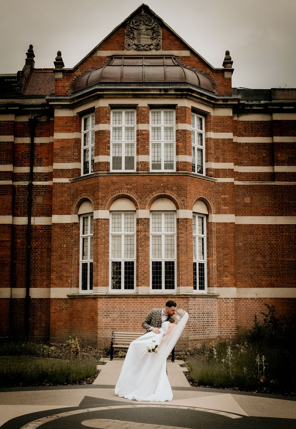 Elegant red brick historic building with white framed bay windows creates a romantic backdrop for wedding portraits.
