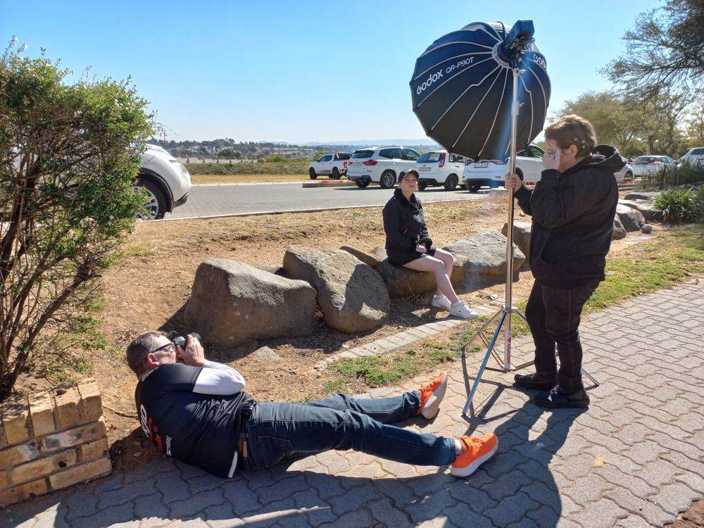 Professional photographer taking pictures of a person lying on brick pathway with lighting equipment and reflector setup.