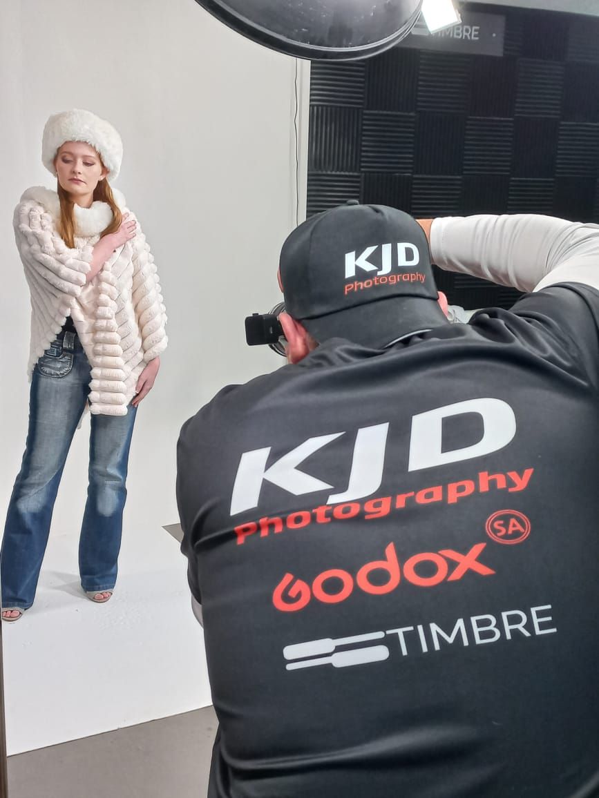Behind-the-scenes photo of KJD Photography studio shoot with photographer wearing branded gear and lighting setup.