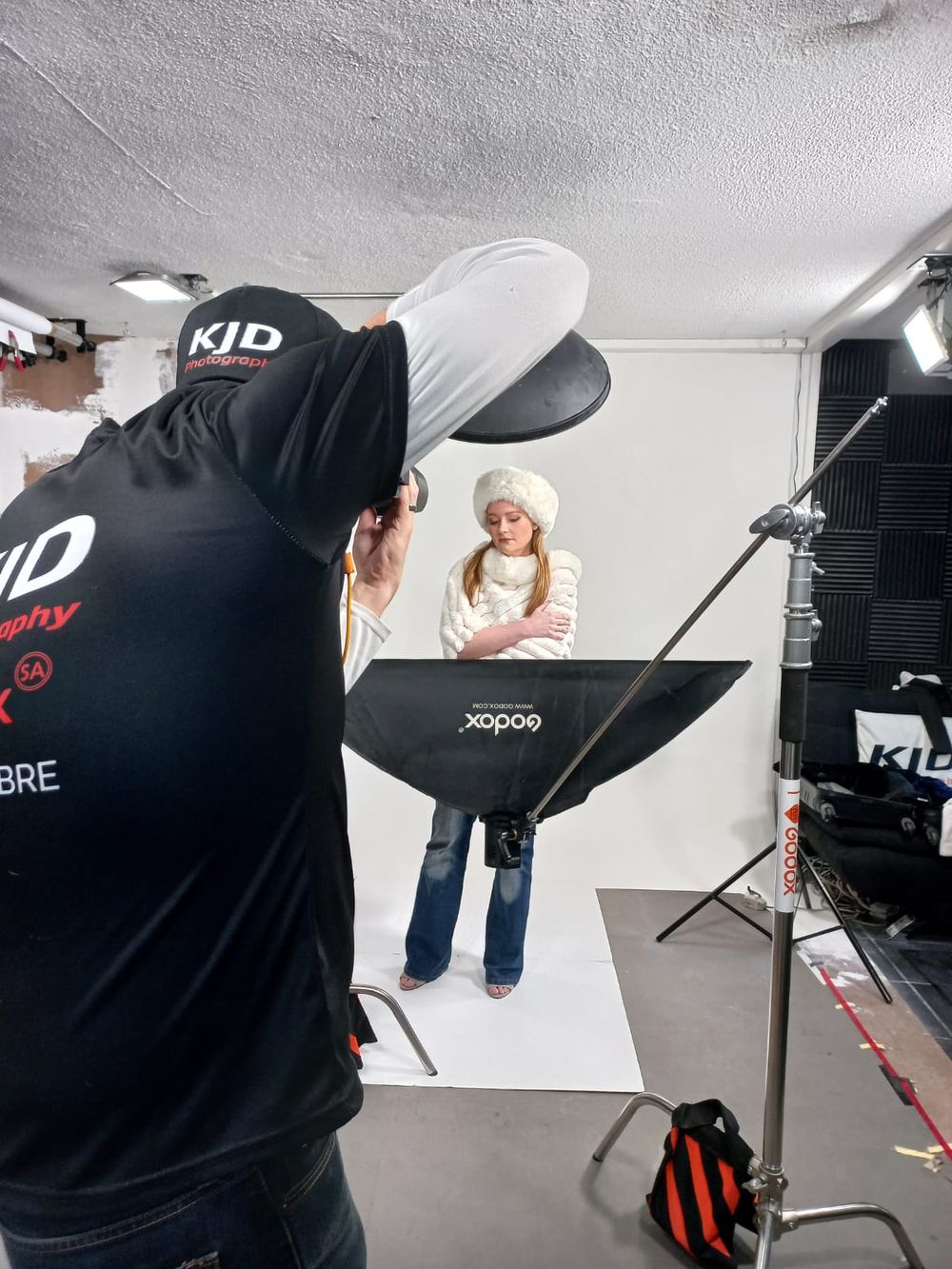 Behind-the-scenes photo of a professional studio photo shoot with lighting equipment and photographer in black shirt.