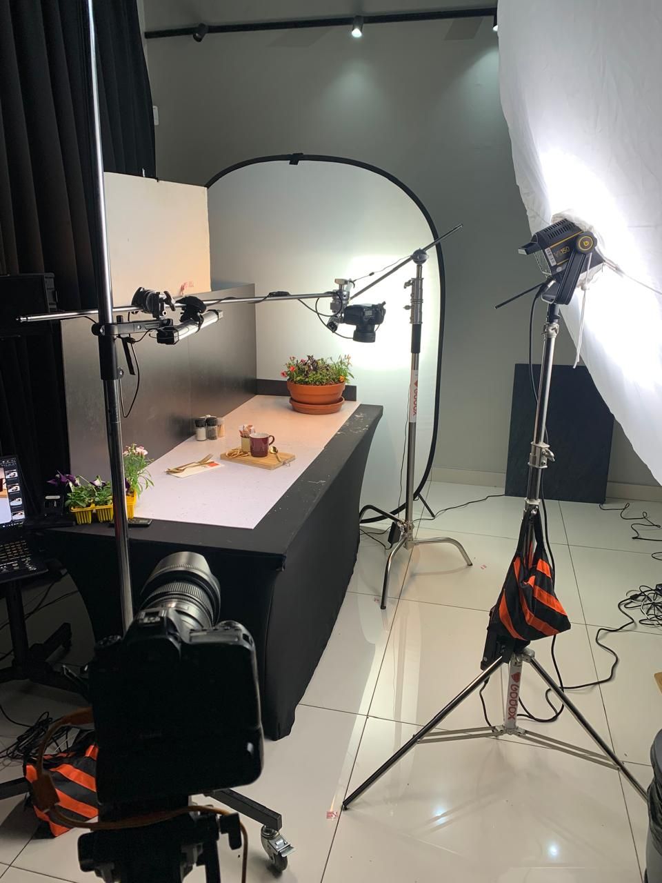 Professional photo studio setup with lighting equipment and small objects on white table for product photography.