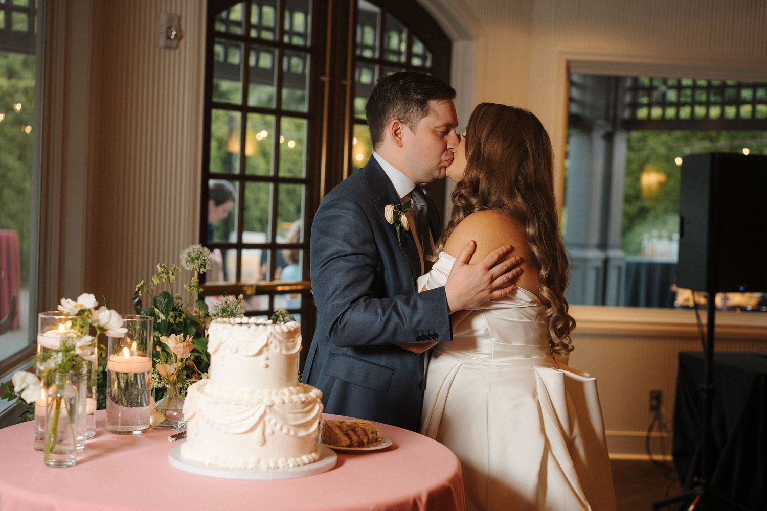 Two elegant wedding cakes decorated with flowers sit atop white tables at an intimate reception venue.