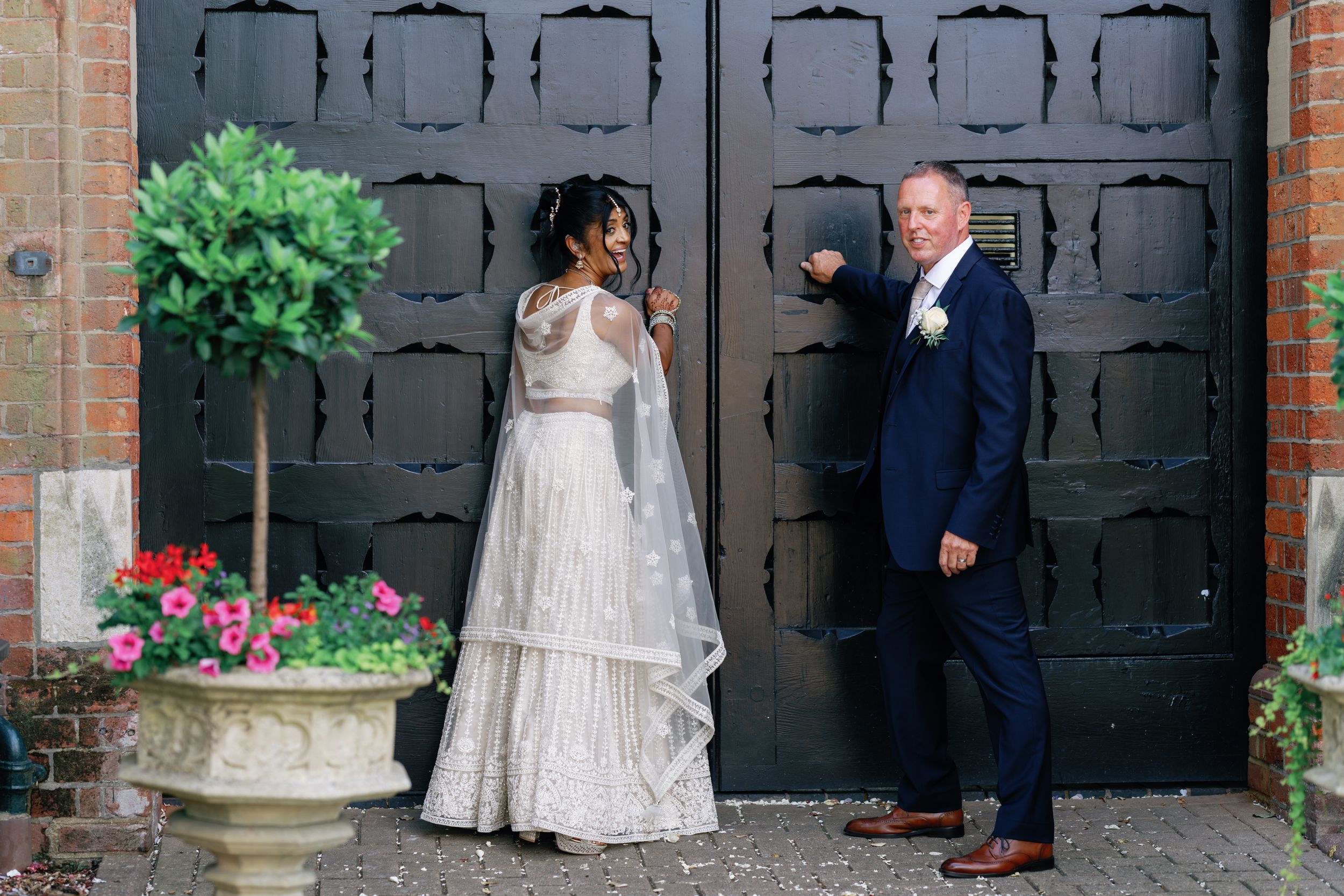 A couple poses by a black ornate door with a decorative planter during their wedding.
