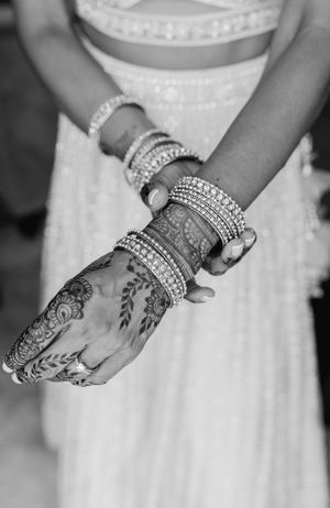A close-up of an intricate henna design and bangles on a bride's hand.